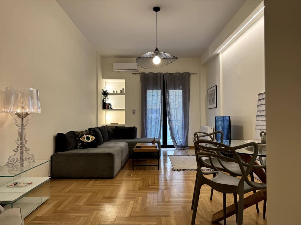 Bright living room of a Kolonaki apartment with a corner sofa, herringbone parquet and a dining table