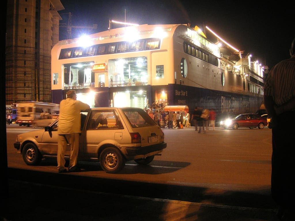 Passengers and cars boarding a lit Blue Star ferry at Piraeus after dark.