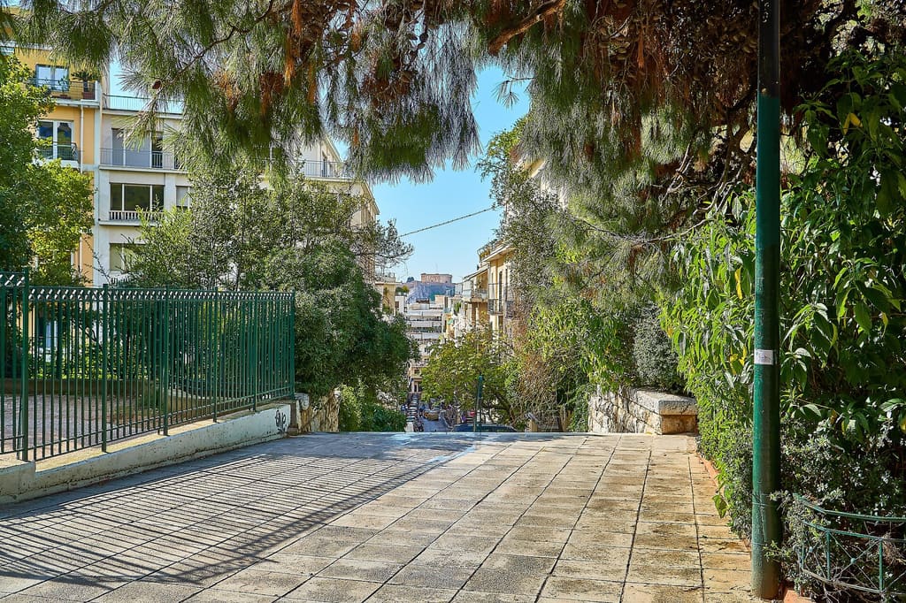 Pine-shaded street sloping down from Dexameni Square in Kolonaki, with the Acropolis in the distance